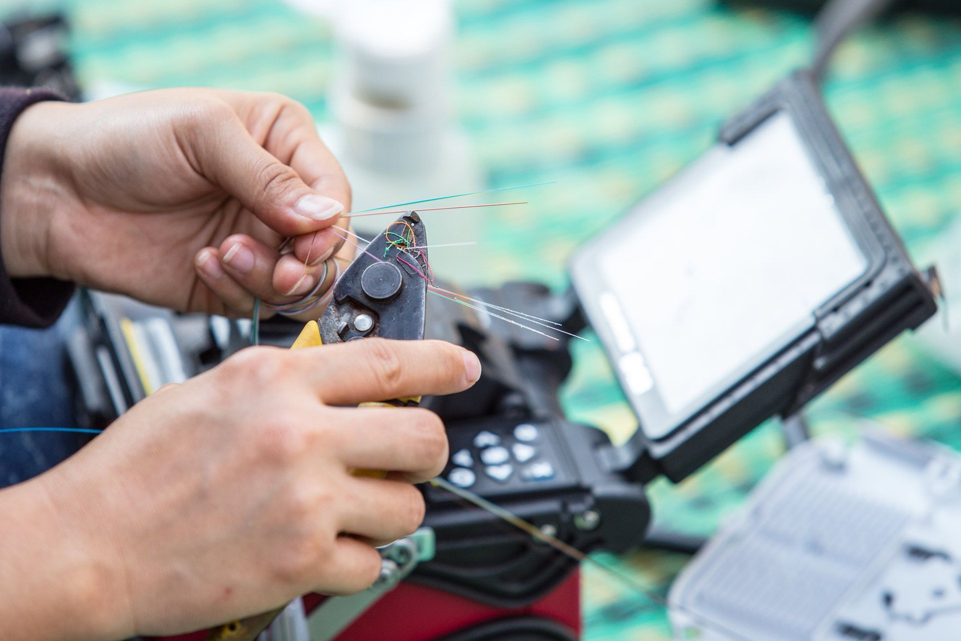 Person splicing fiber optic cables using a fusion splicer outdoors.