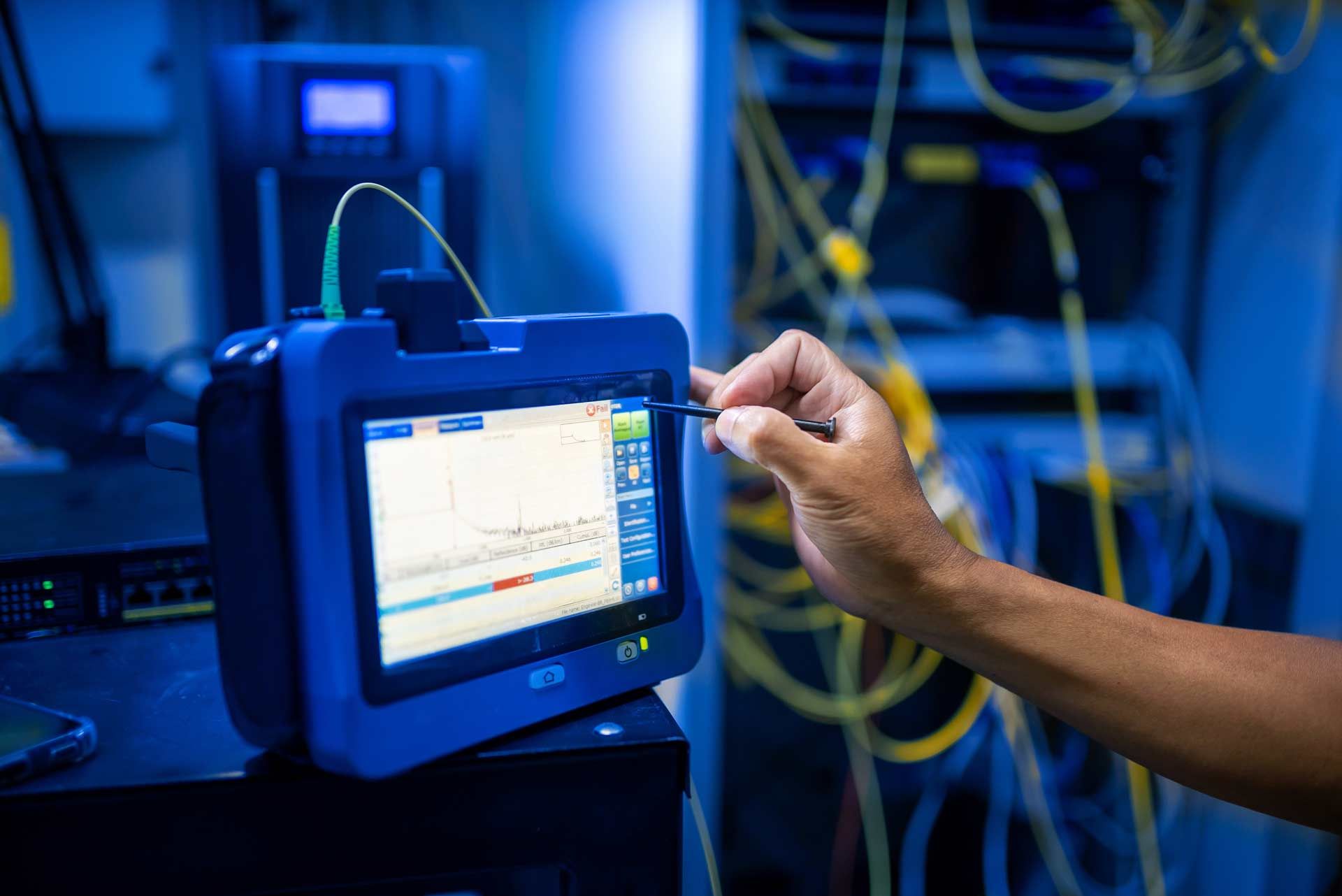 A technician using a blue device to analyze data in a server room with cables.