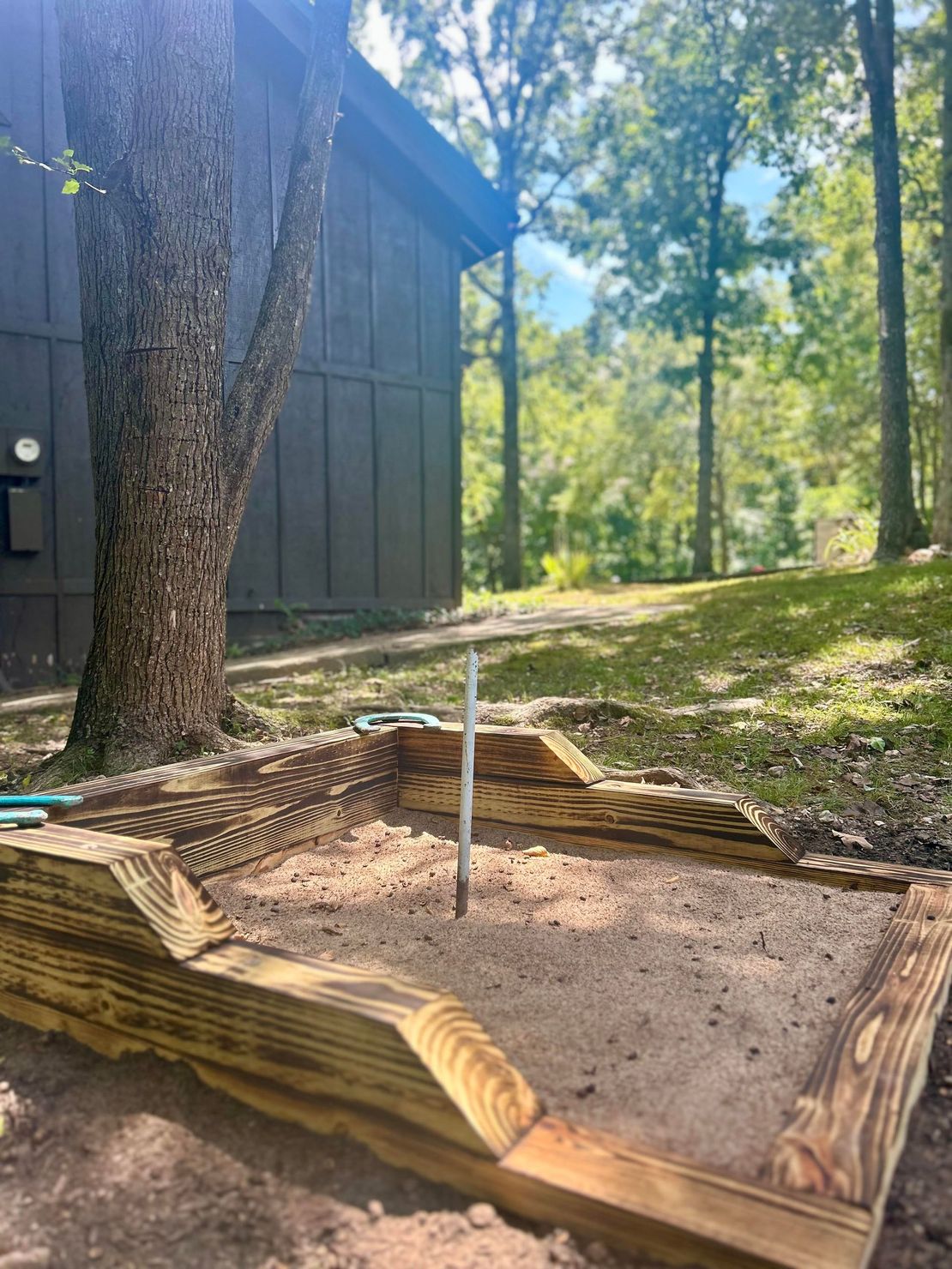 A wooden sandbox is sitting in the dirt in front of a house.