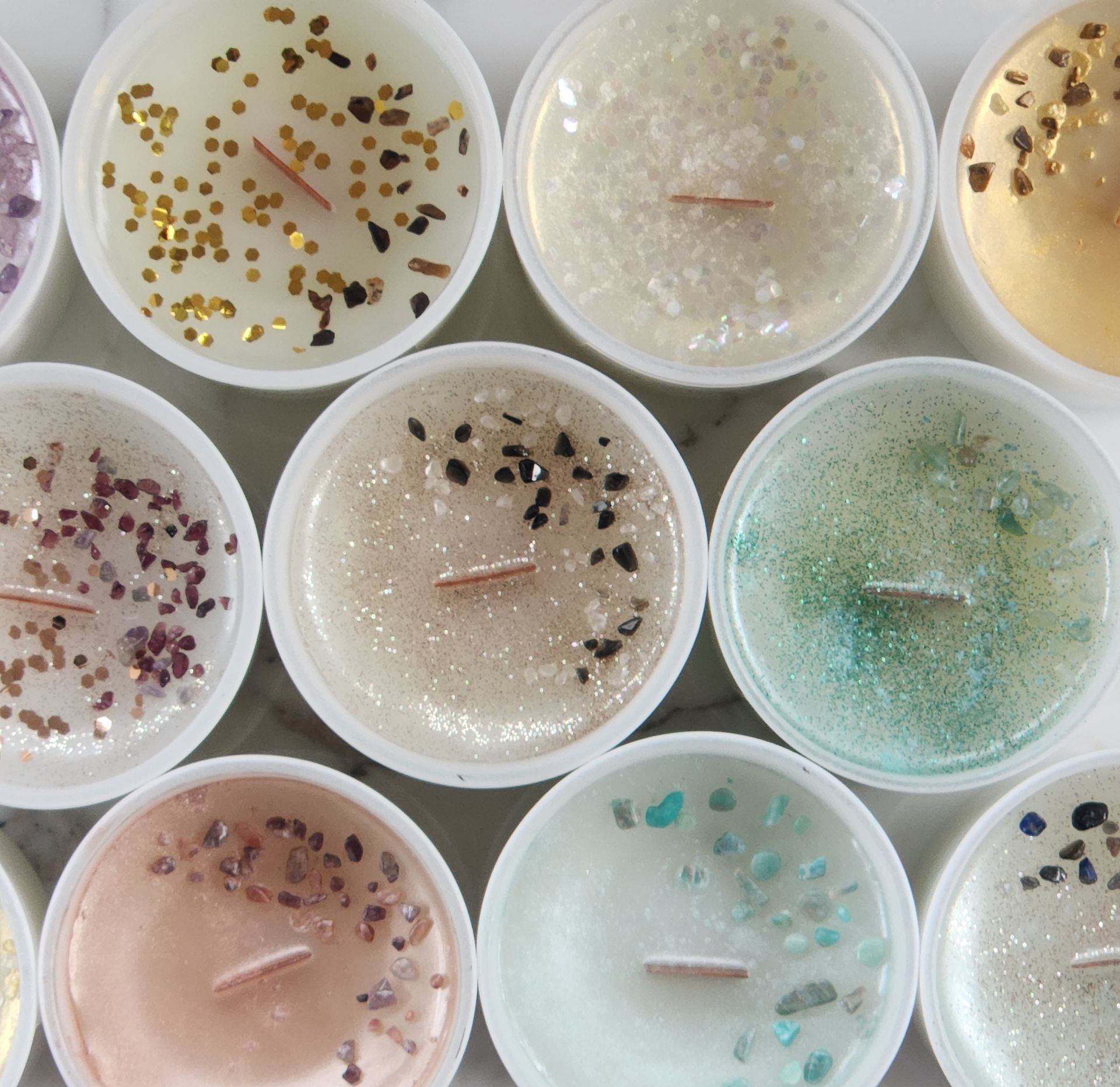 Close-up of colorful, decorative soy candles in white containers, each with glitter and gemstones.
