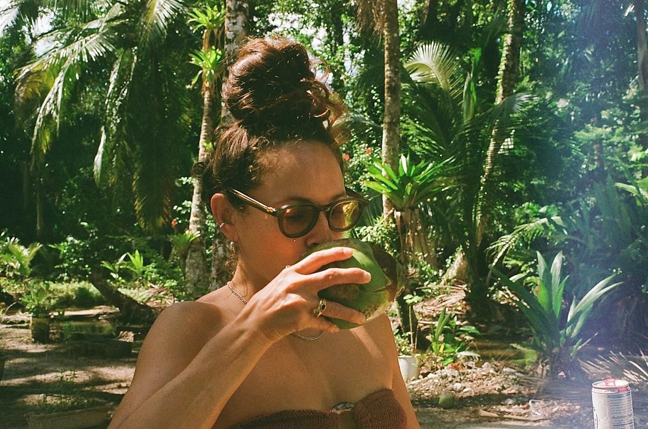A woman is drinking from a coconut in the jungle.