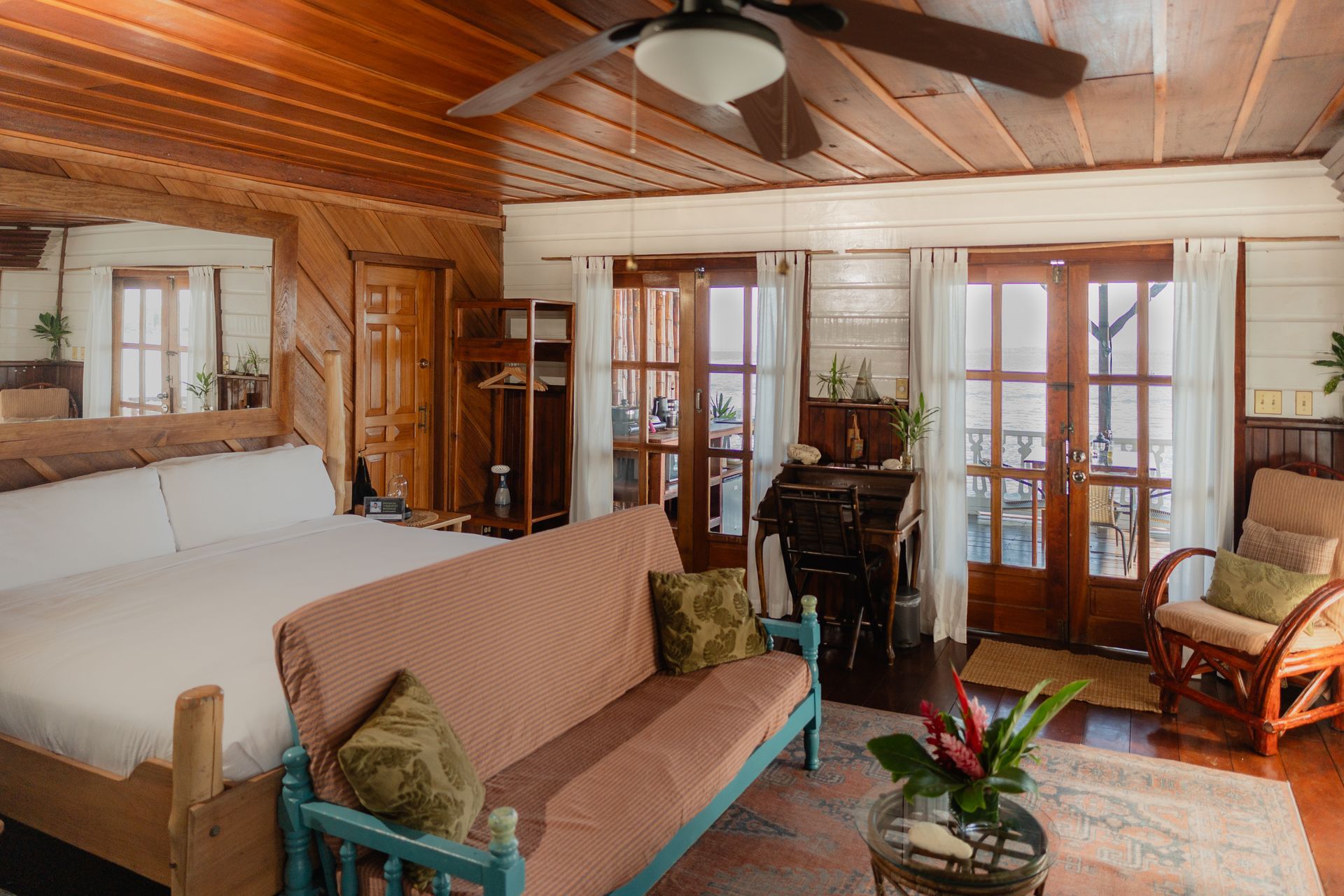A living room with a bed , couch , chair and ceiling fan.