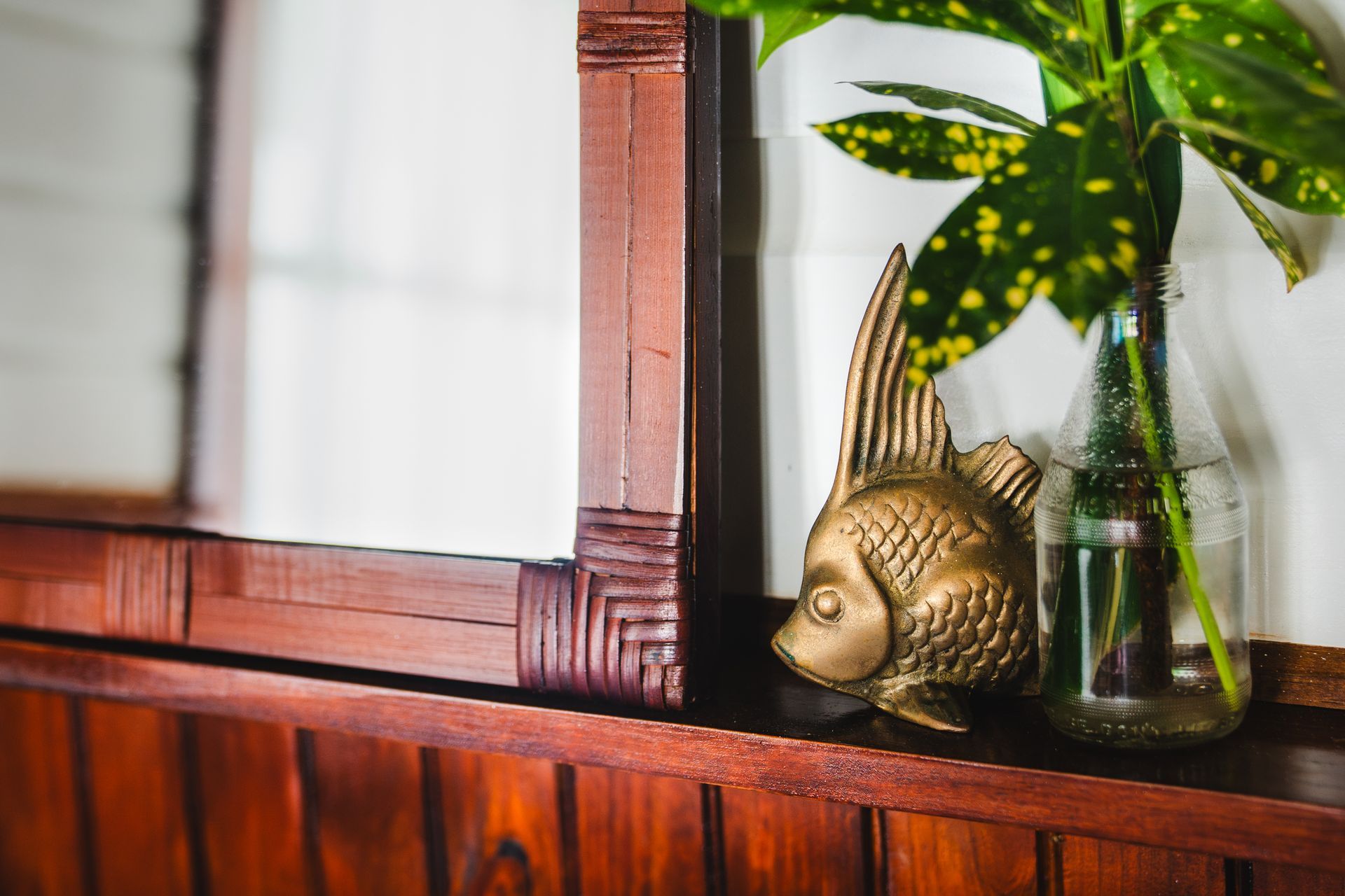 A statue of a fish is sitting on a wooden shelf next to a vase of flowers.