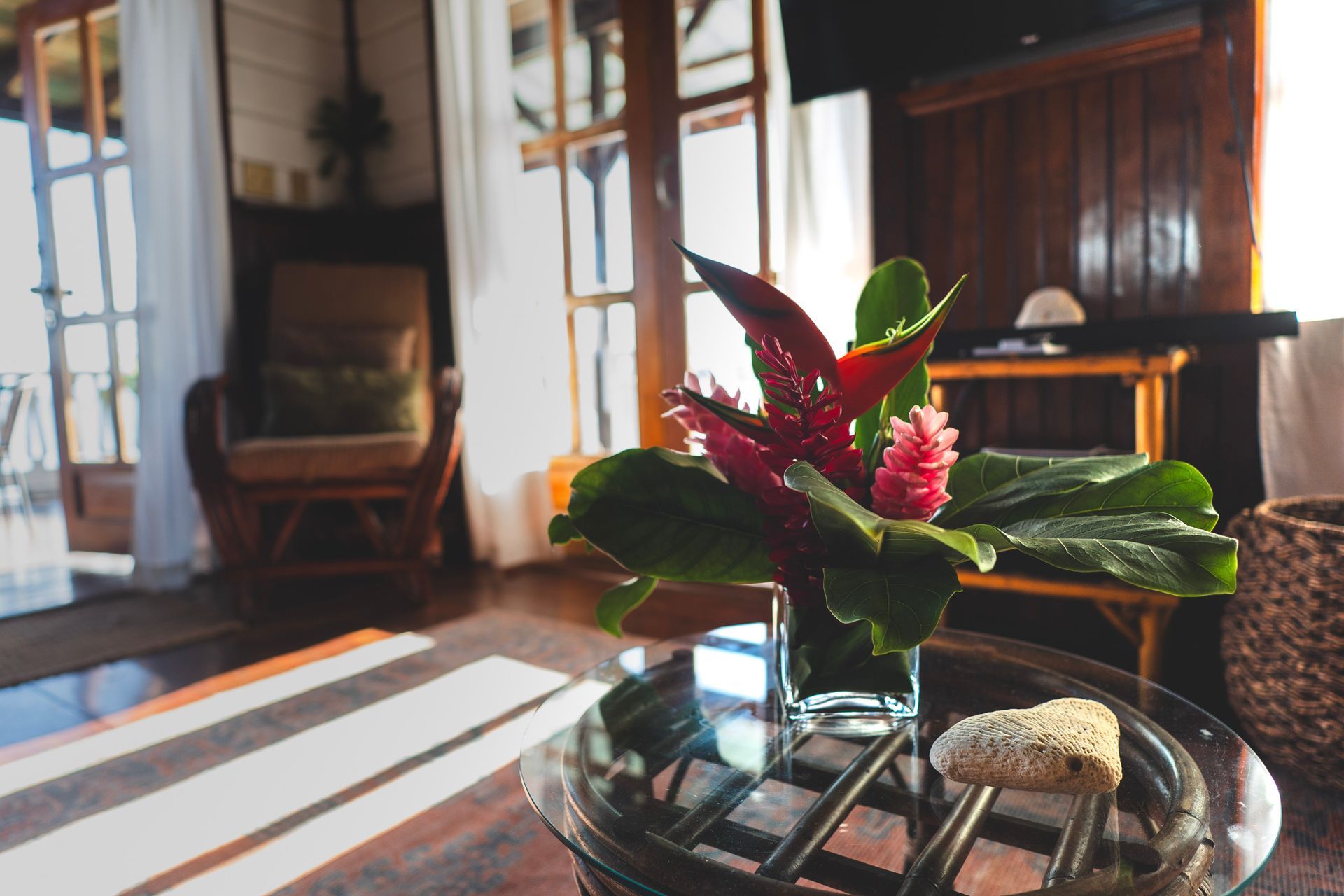A vase of flowers is on a glass table in a living room.