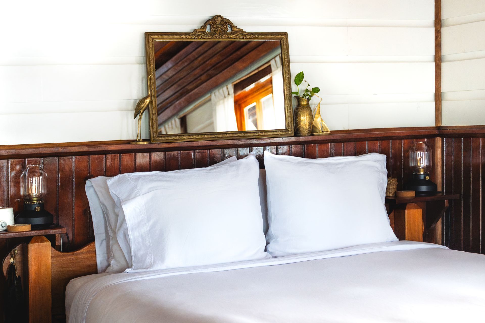 A bed with white sheets and pillows and a mirror above it.