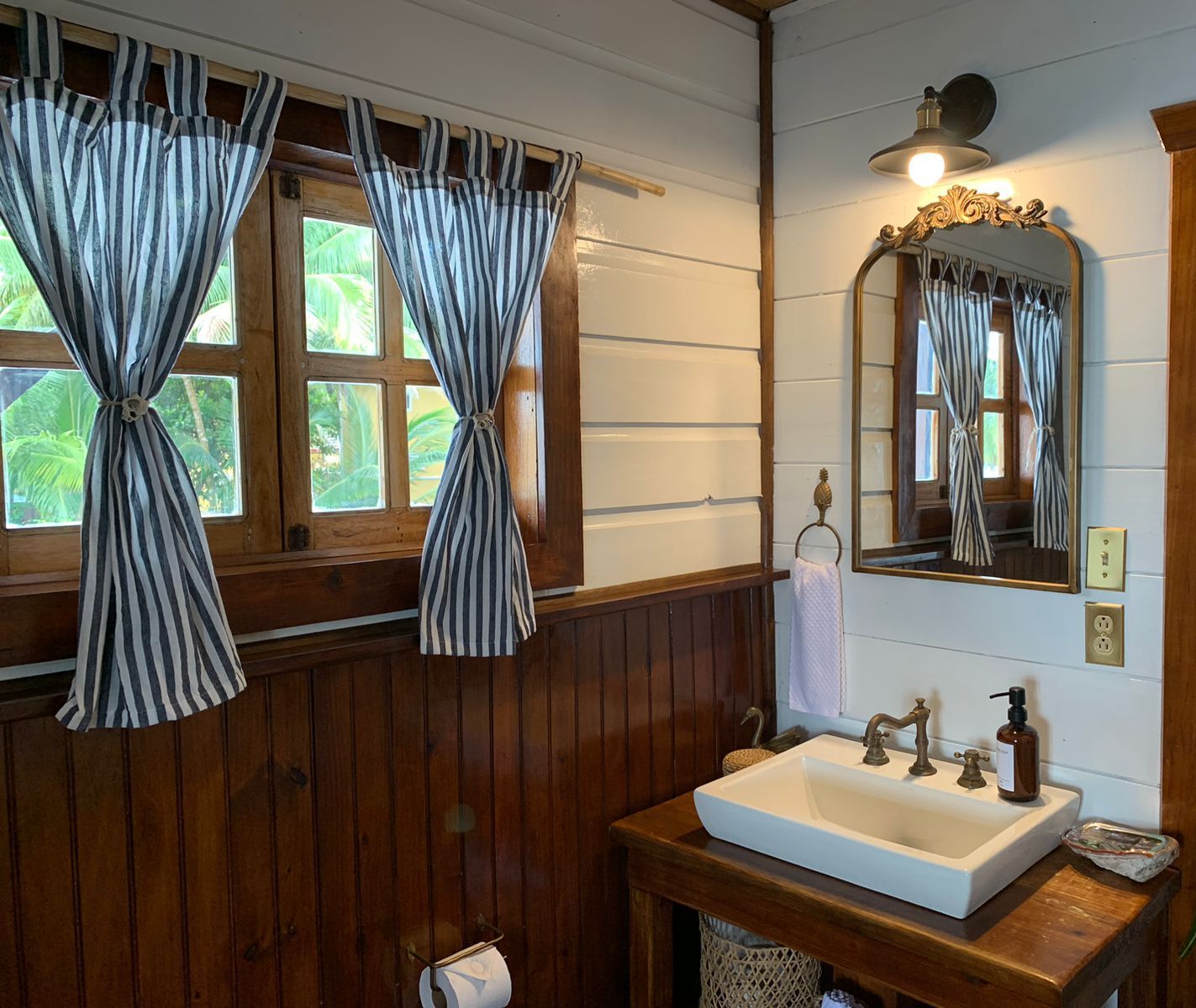 A bathroom with a sink a mirror and striped curtains