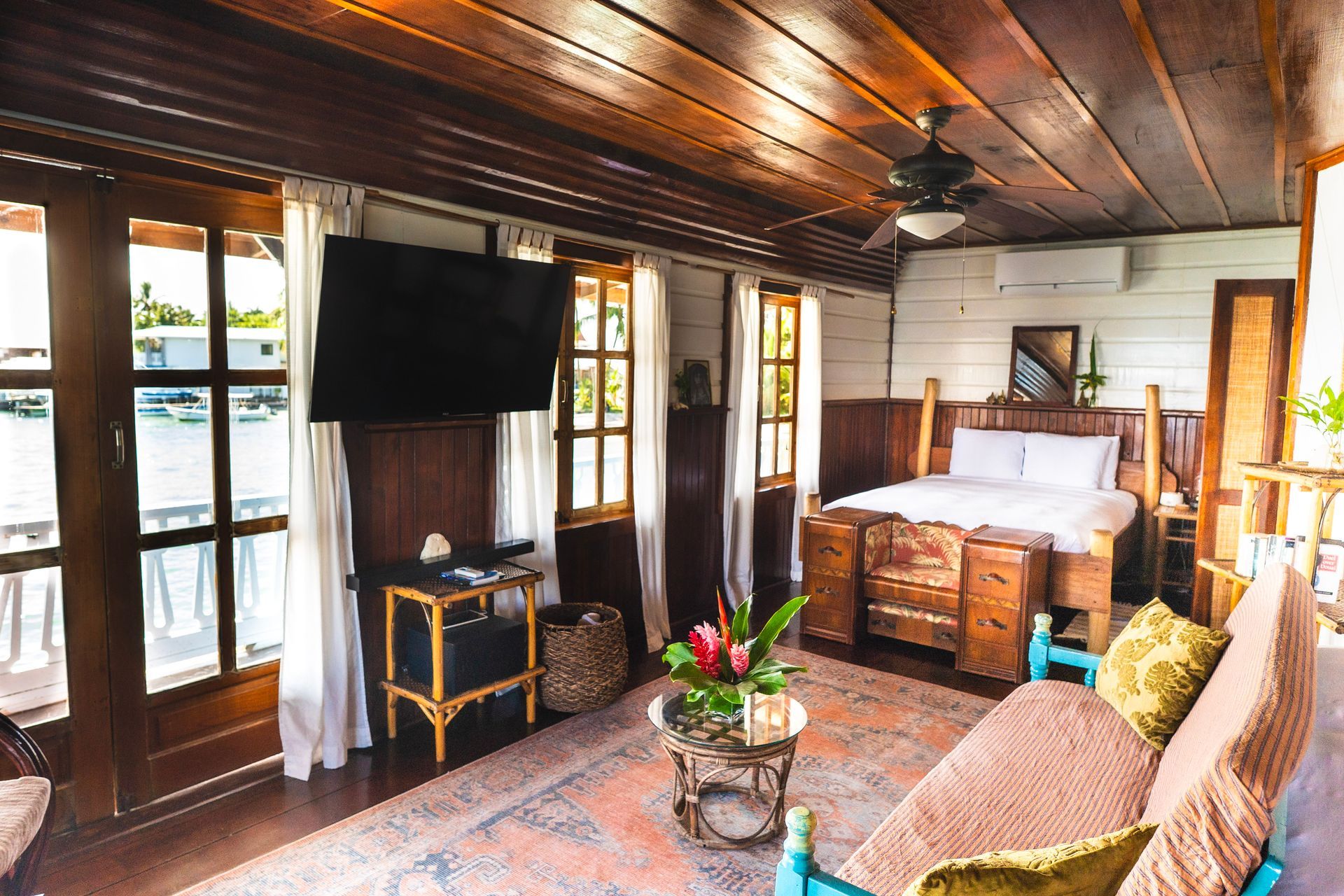 A living room with a bed , couch , television and ceiling fan.