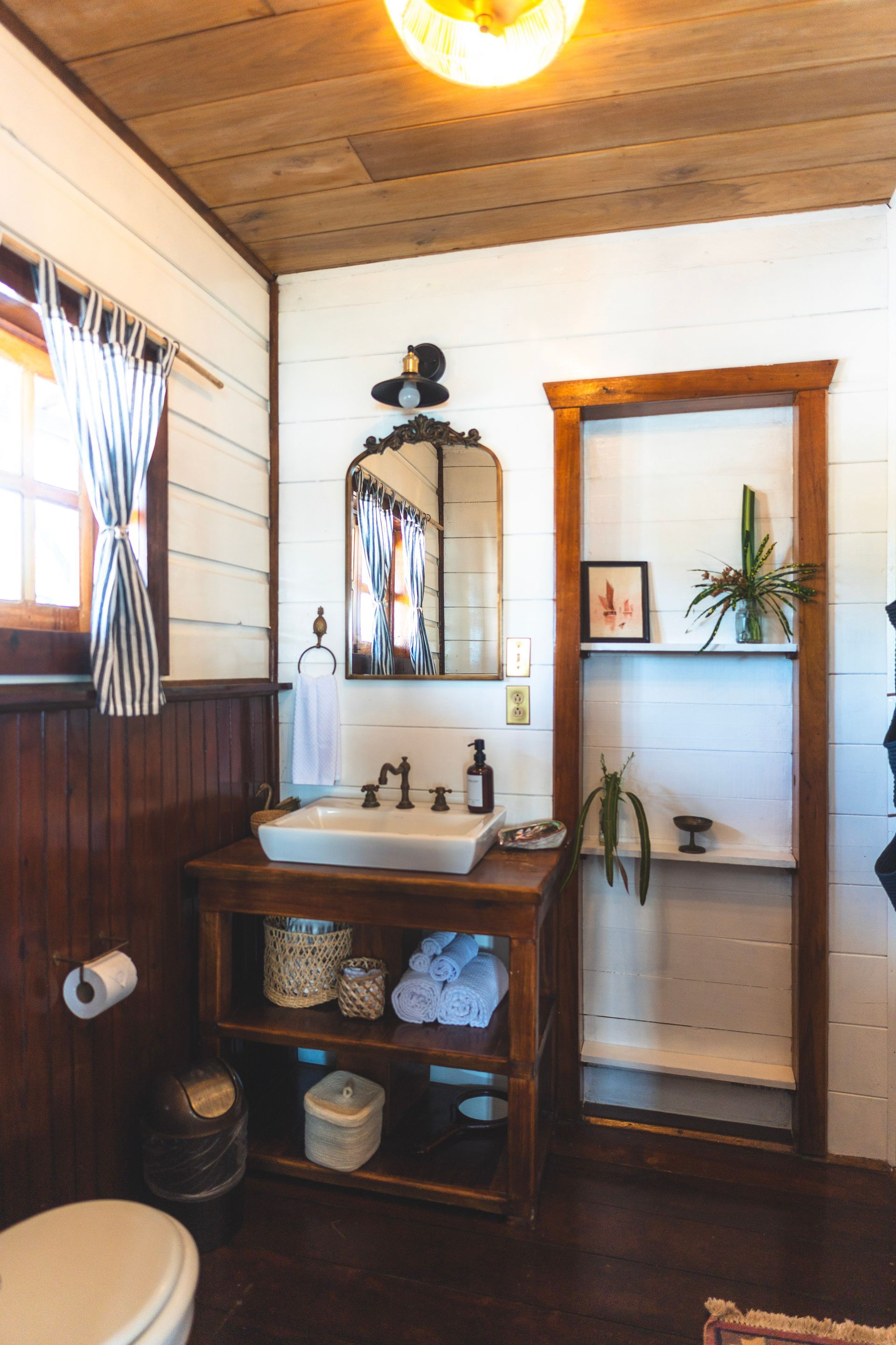 A bathroom with a toilet , sink , mirror and shelves.