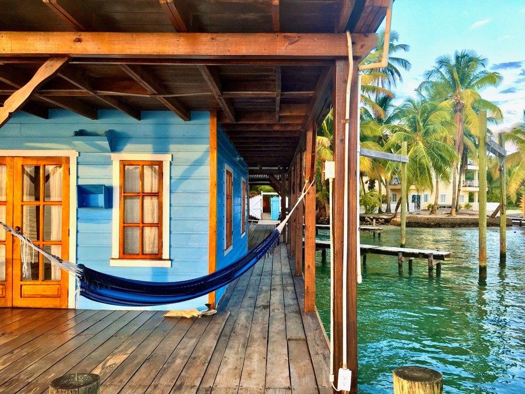 A blue house with a hammock on the porch next to a body of water.