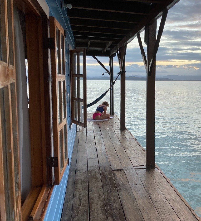 A person sits in a hammock on a wooden deck overlooking the ocean