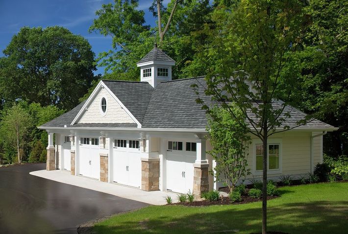 White garage with three bays, stone accents, and cupola, set in a green, wooded area.