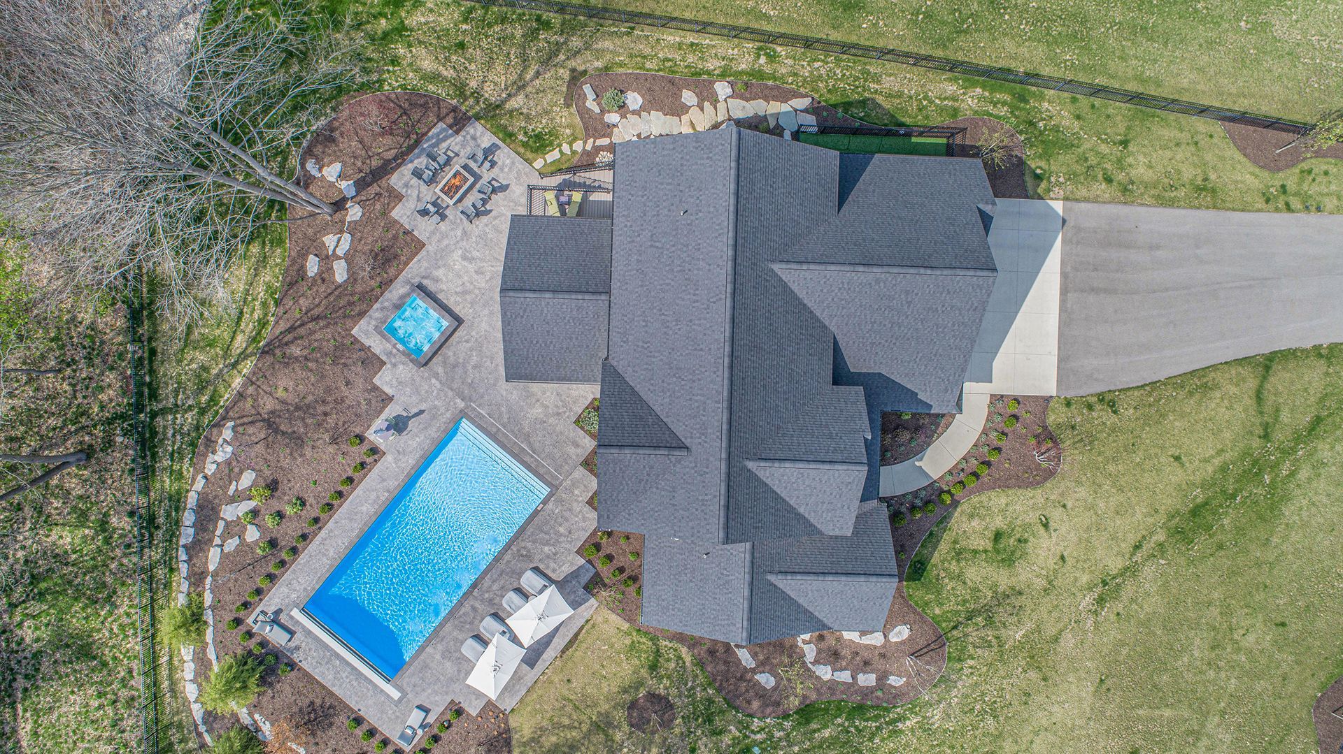 Overhead view of a house with a pool, hot tub, patio, and driveway on a grassy property.