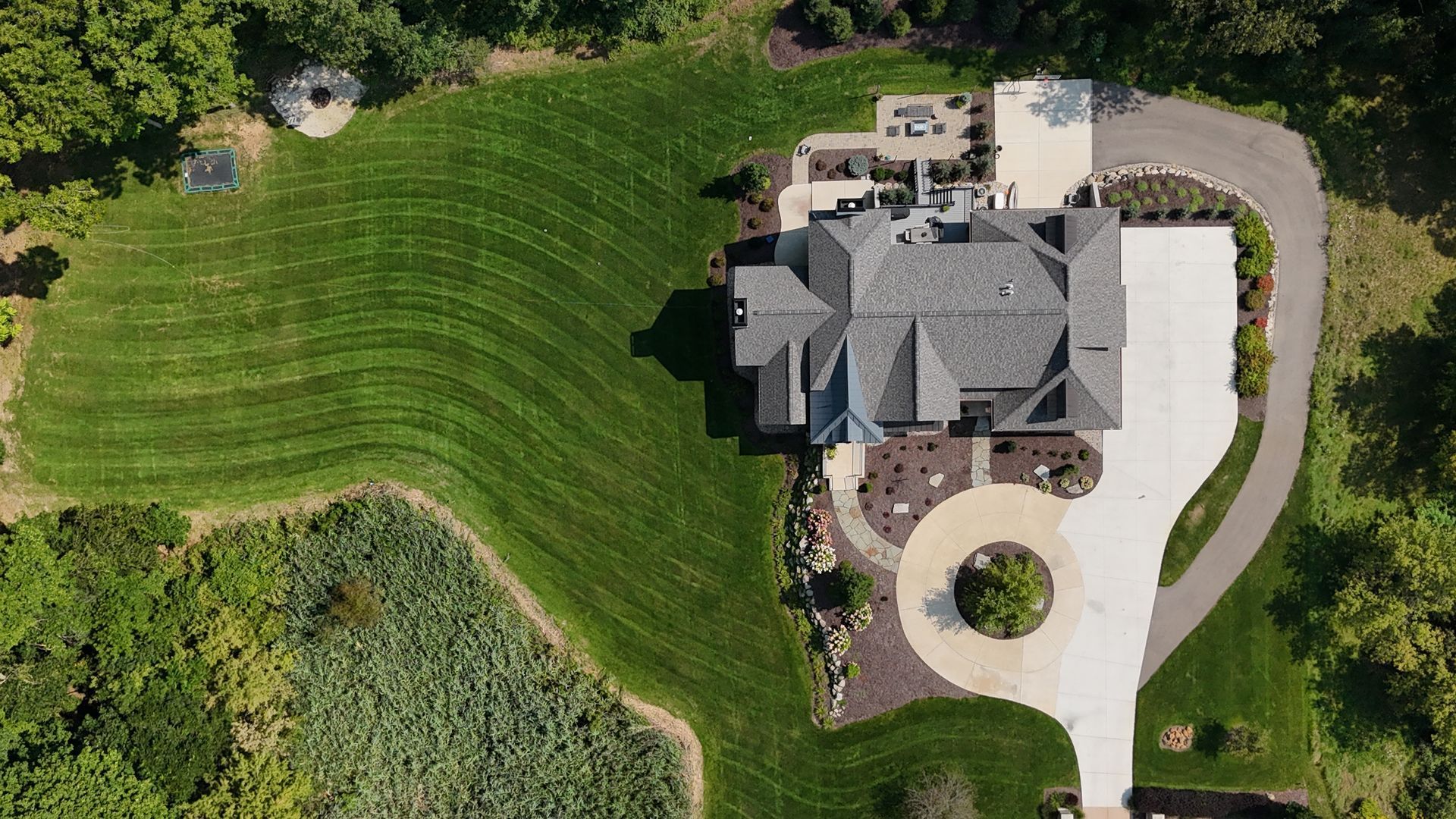 Aerial view of a gray-roofed house with a winding driveway and landscaped yard.
