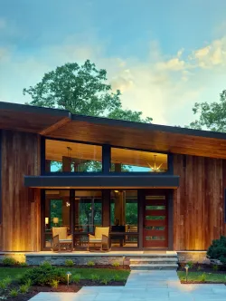 Modern wood-clad home exterior with glass windows and door, stone pathway, and manicured landscaping.