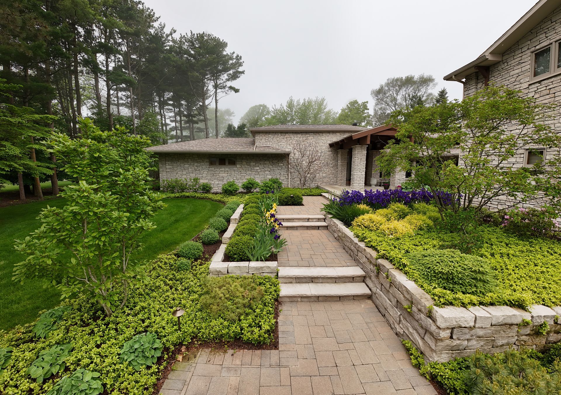 Stone house with a brick pathway and landscaped gardens; cloudy day.