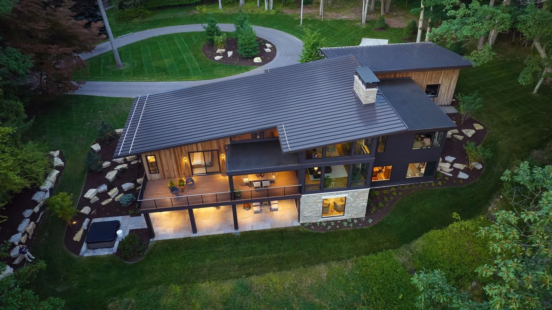 Modern home nestled in greenery, with a sloped roof and large windows. Driveway curves around the house.