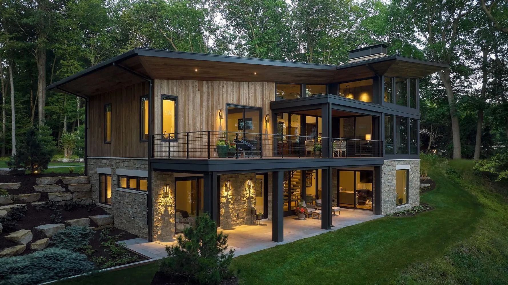 Modern multi-level home with stone and wood exterior, surrounded by trees.