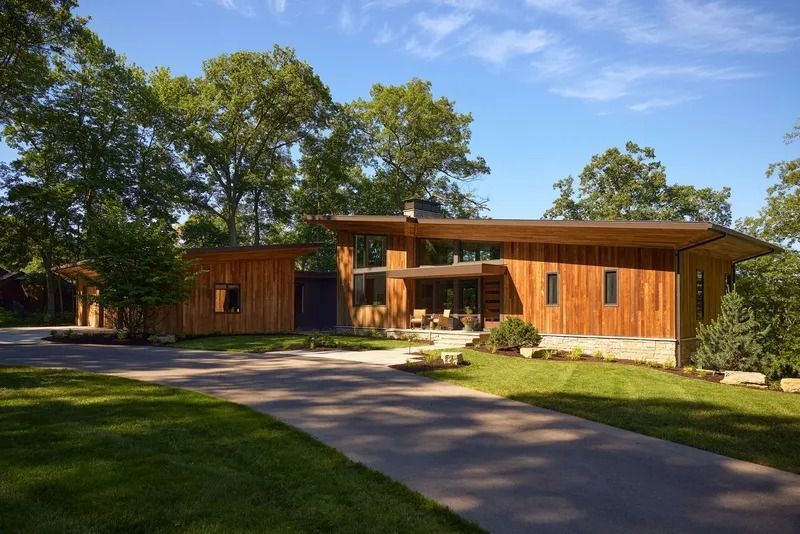 Modern wood-clad house with angled roof, driveway, and lush green lawn under a sunny blue sky.