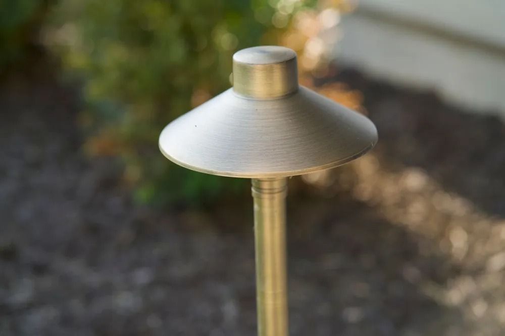 Bronze landscape path light with a mushroom-shaped head in a garden setting.
