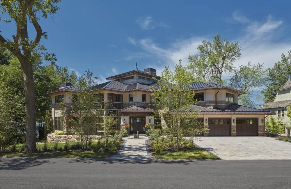 Large multi-story home with stone and wood exterior, three-car garage, and tiled roof, on a sunny day.