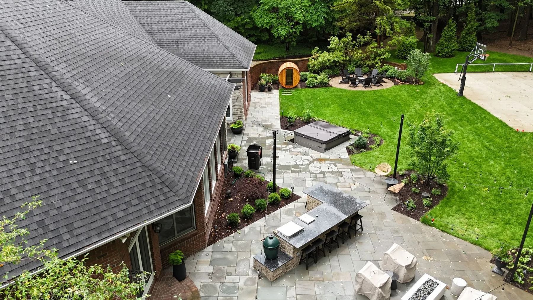 Aerial view of a home's backyard with patio, seating, grill, and green lawn.