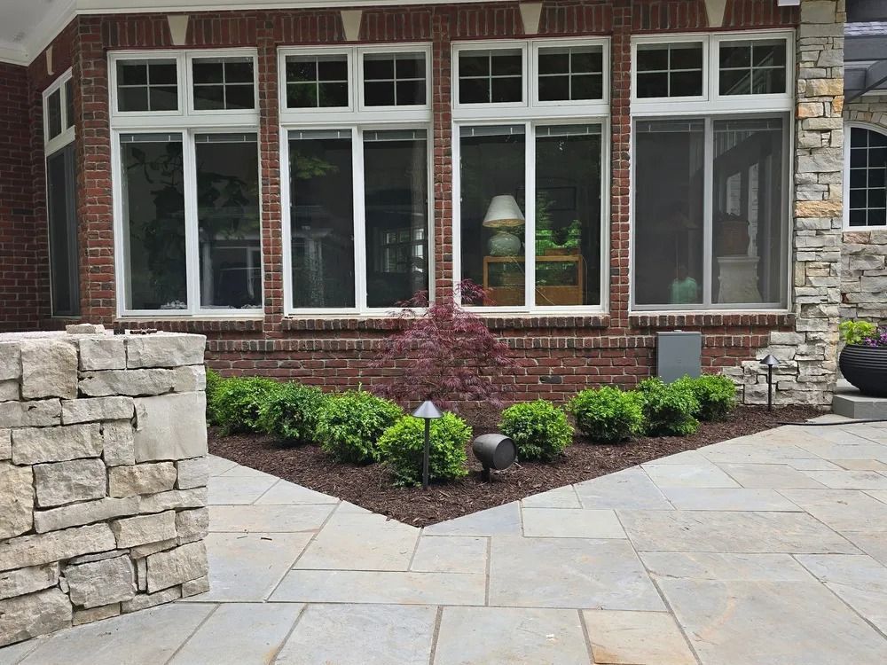 Stone patio with brick wall and large windows, landscaping, and a stone pillar.
