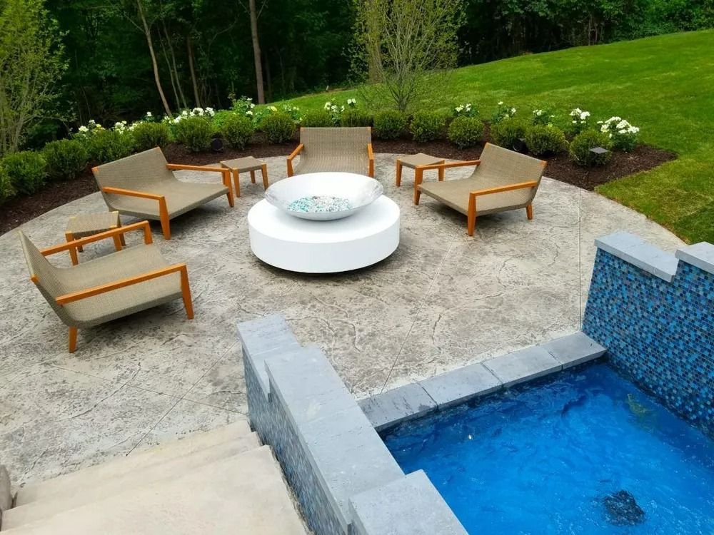 Patio with seating around a white fire pit, small tables, and a pool with waterfall feature.