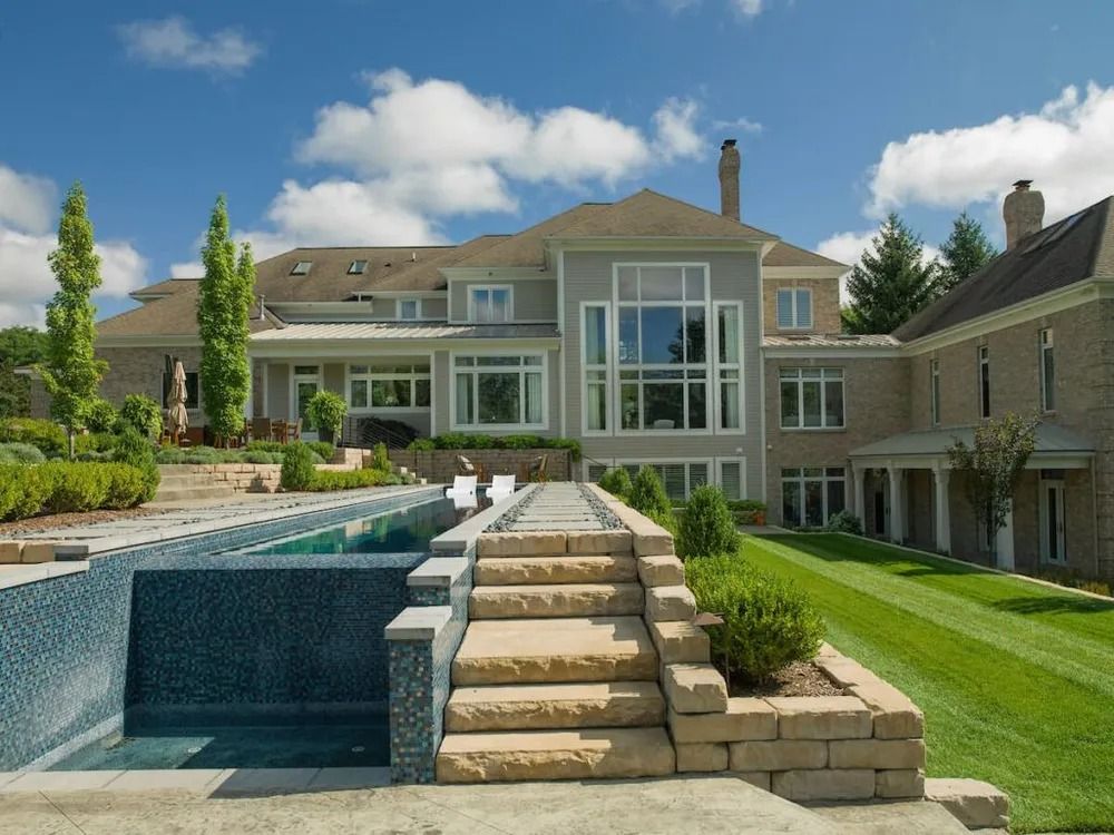 Luxury home with pool and tiered landscaping, under blue sky with clouds.