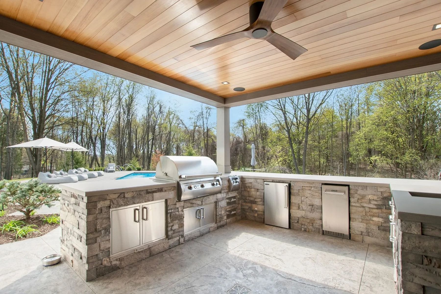 Outdoor kitchen with stone counters, stainless steel appliances, and a wooden ceiling.