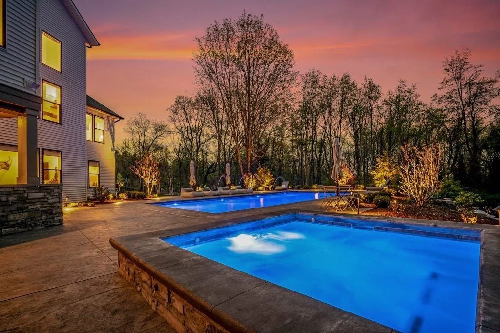 Pools at dusk, illuminated with a house on the left and trees in the background under an orange sky.