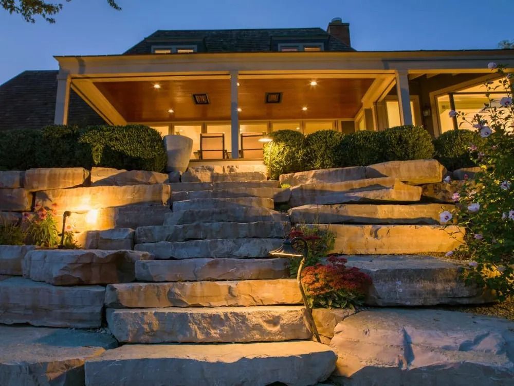 Stone steps lead up to a house with a covered patio, illuminated at dusk.