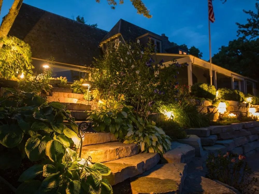 Stone steps with illuminated landscaping leading to a house at dusk.