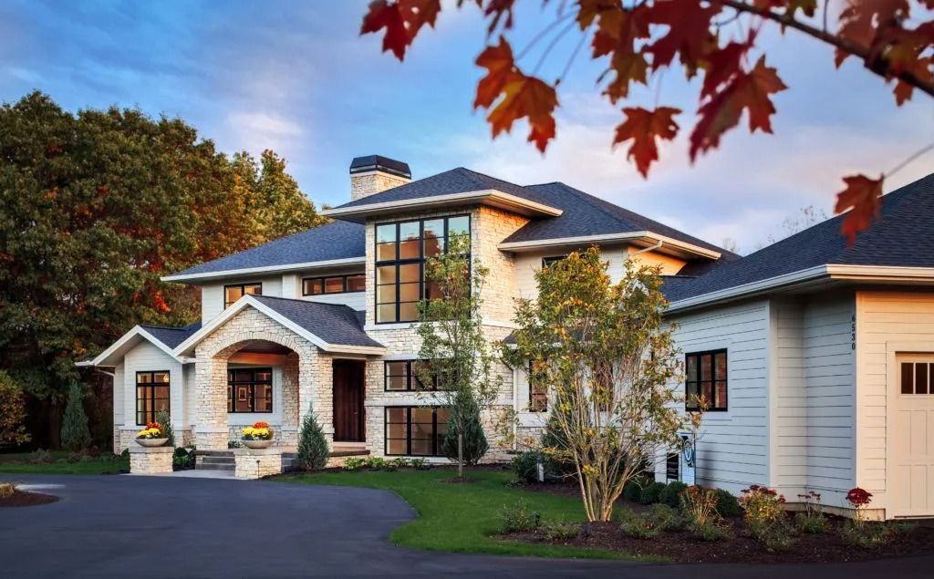 Luxurious white house with black roof, garage, and stone accents, with a driveway and autumn trees.