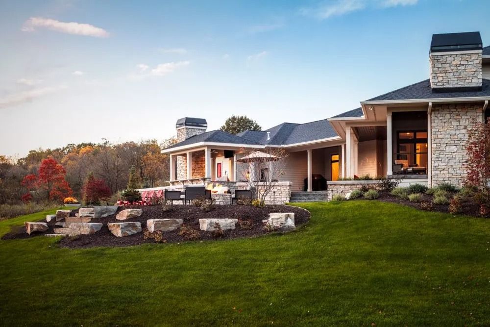 Stone house with porch, chimney, and landscaped lawn on a sunny day.