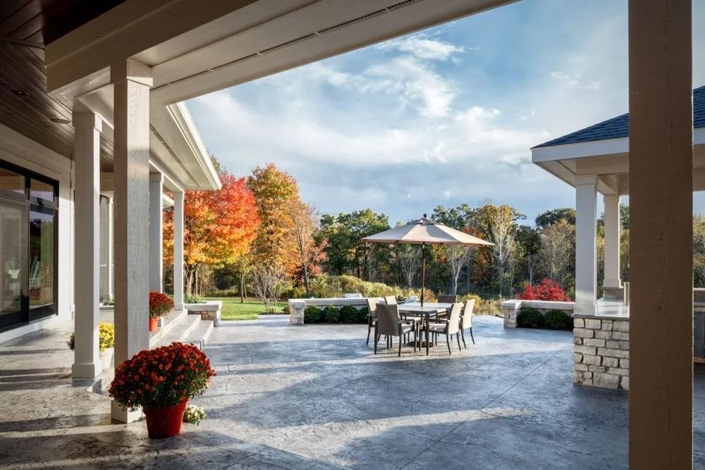 Patio with dining table, umbrella, and fall foliage in background. Overcast sky.