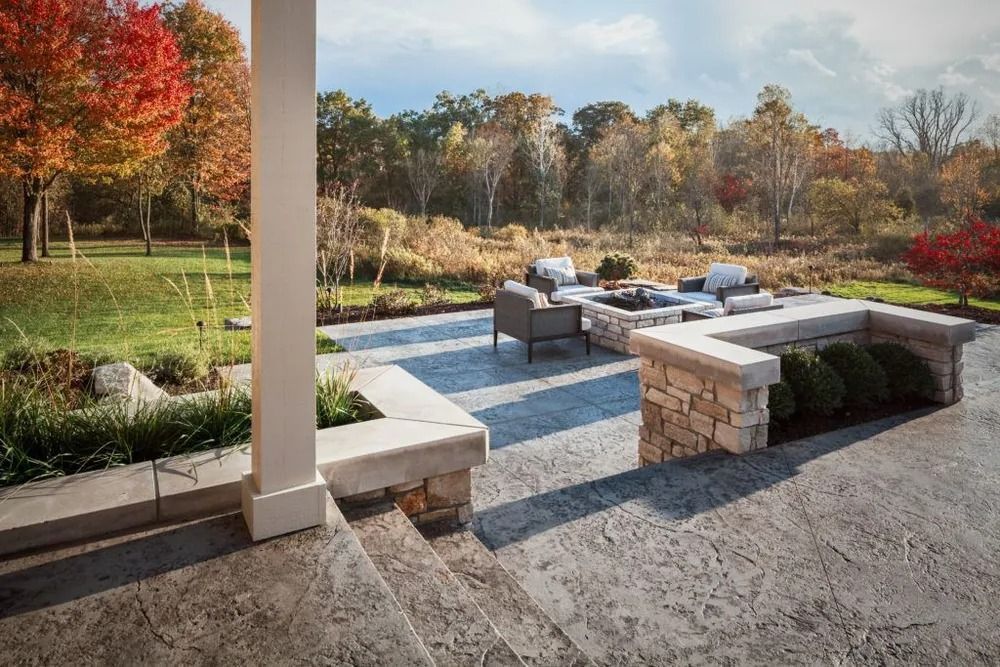 Outdoor patio with fire pit, seating, stone walls, and colorful fall foliage.