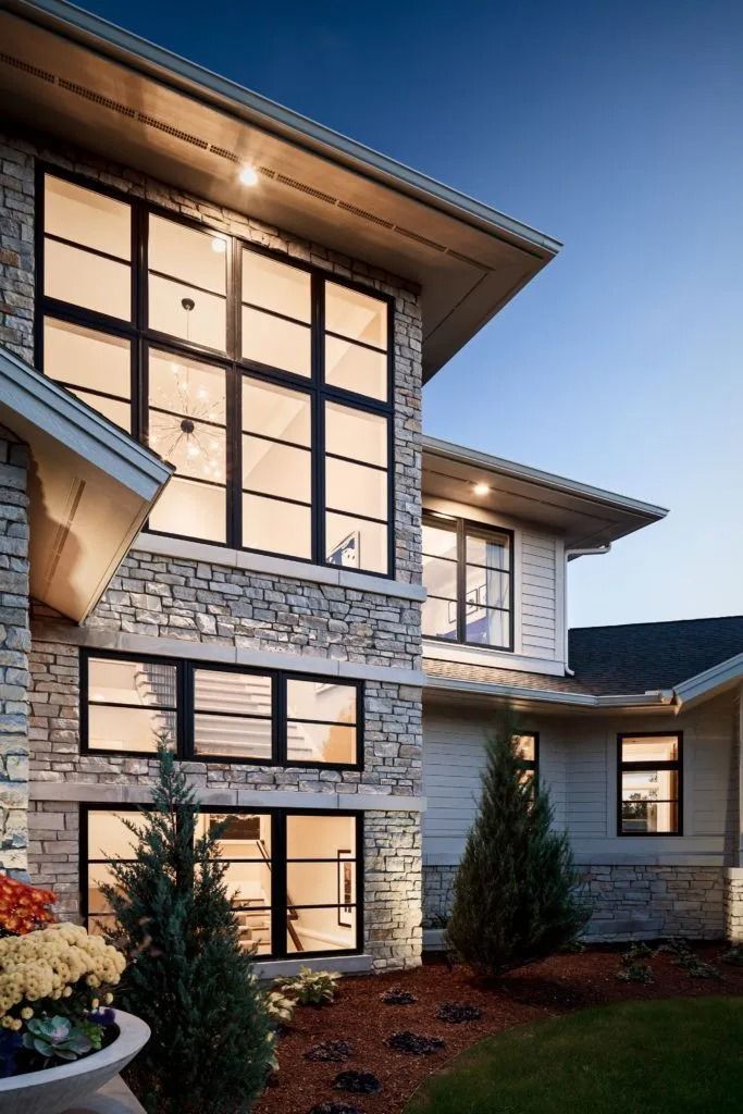 Two-story house with stone and siding facade, large windows, and evening sky.