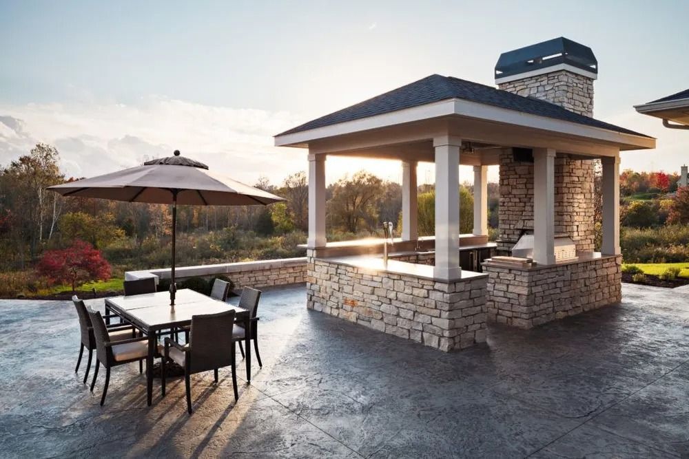 Outdoor kitchen and dining area with stone accents, a table, and umbrella.