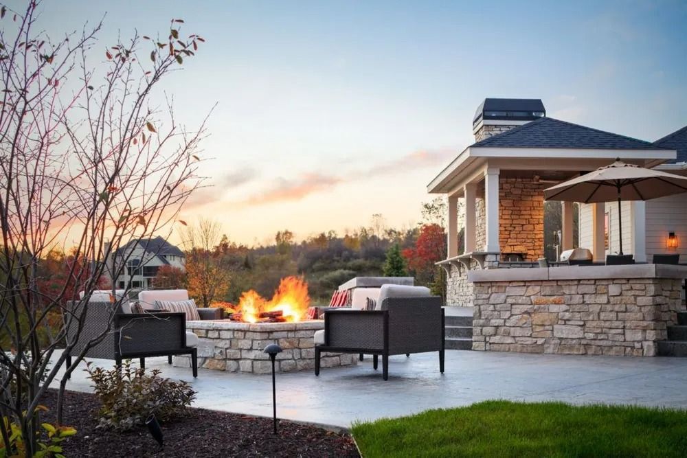 Outdoor patio with fire pit, seating, stone wall, and gazebo at dusk.