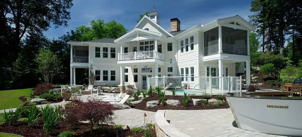 White house with screened porch, overlooking a stone patio and landscaping, boat in foreground.