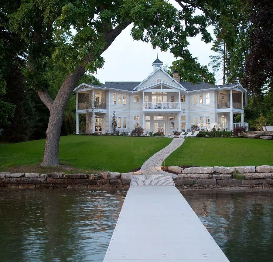 White lakeside house with a long dock and green lawn.