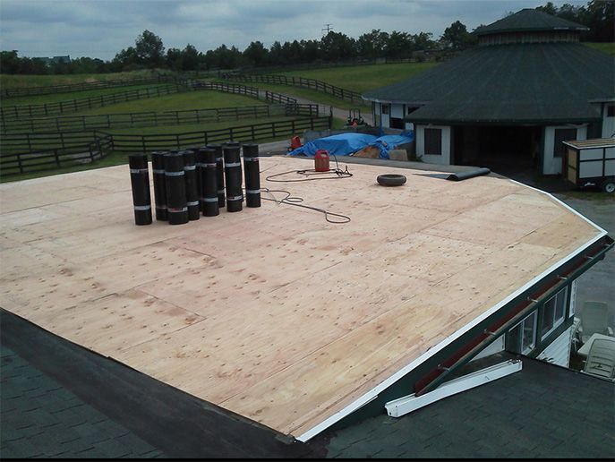 Roofing work on a building, with stacks of rolled roofing material. Surrounding landscape visible.