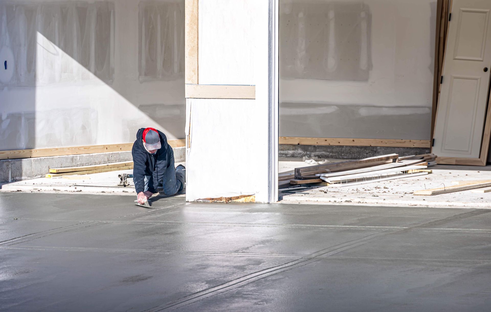 Person kneeling, smoothing wet concrete floor in a garage under construction.