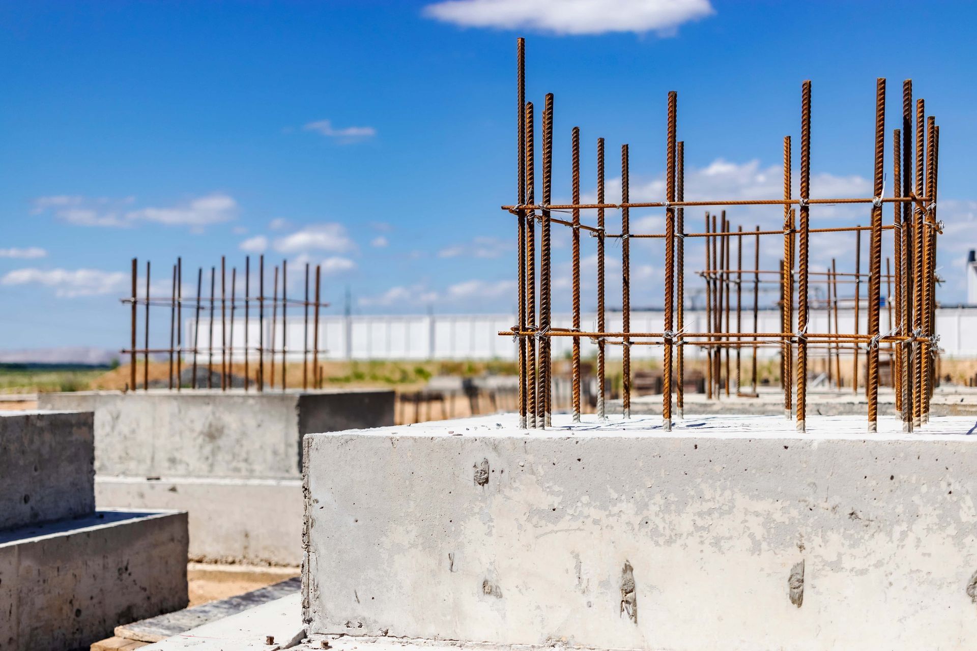 Concrete foundation pillars with rebar framework, blue sky background.