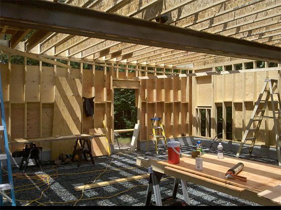 Interior view of a building under construction, showing wooden framing, exposed beams, and construction materials.