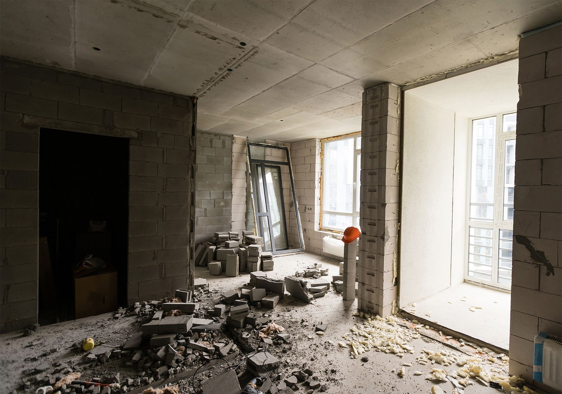 Interior of a room under construction, with exposed concrete block walls and debris on the floor.