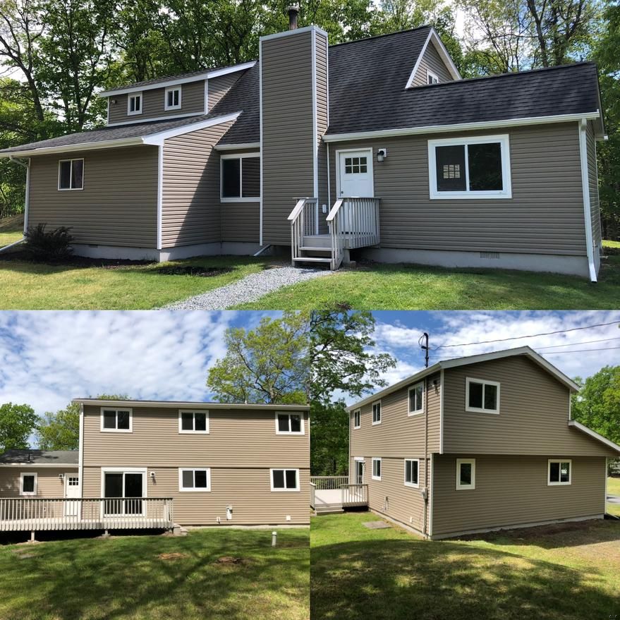 Tan-sided two-story house with white trim, a dark roof, and a stone path in a grassy setting.