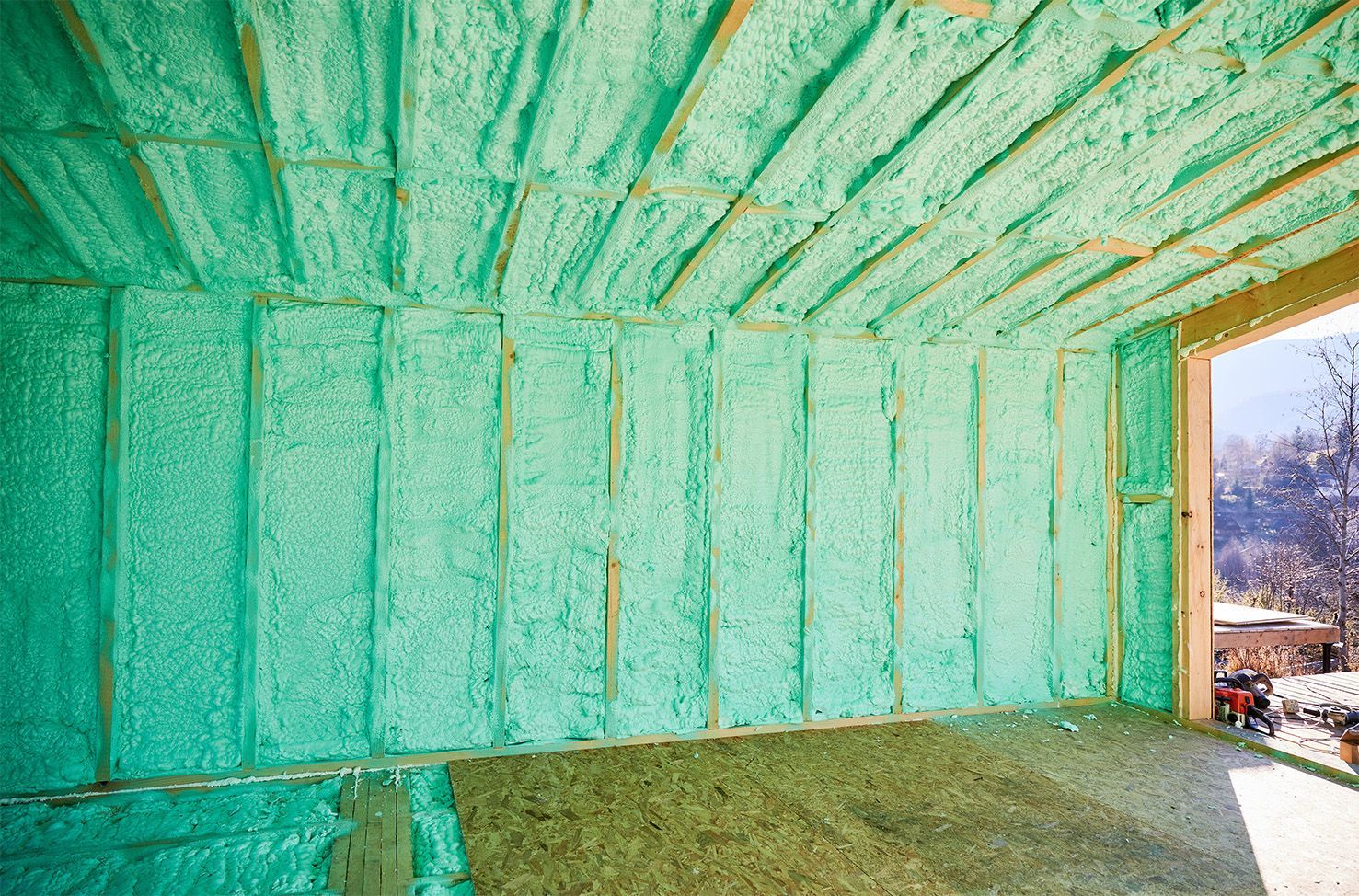 Interior of a room with green spray foam insulation applied to walls and ceiling, framing visible.