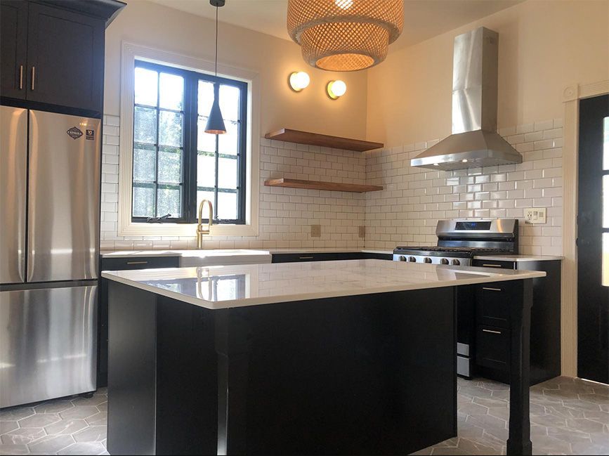 Modern kitchen with black island, stainless steel appliances, and white subway tile backsplash.