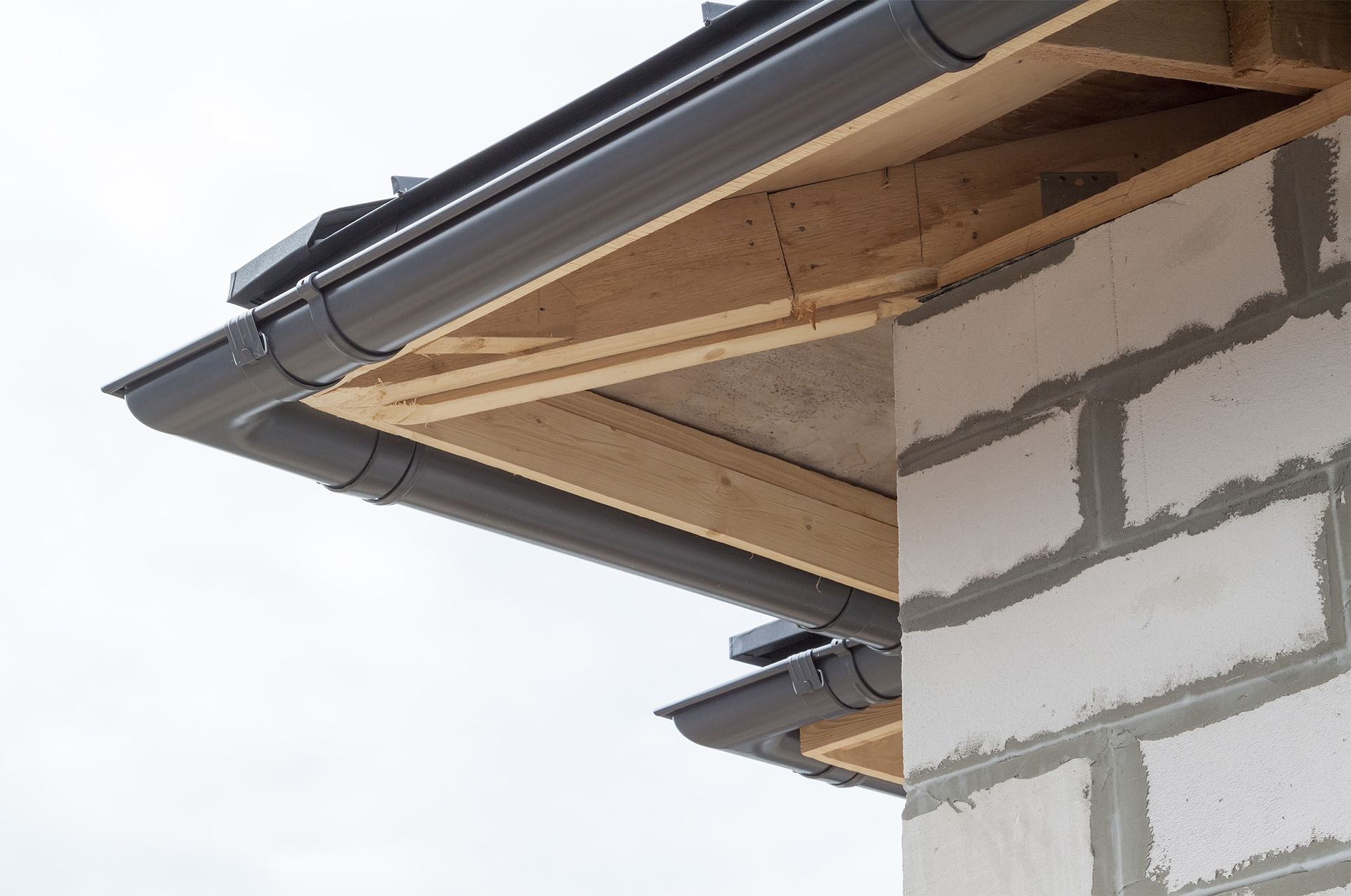 Gray gutters attached to a building under construction, showing wooden beams and concrete blocks.